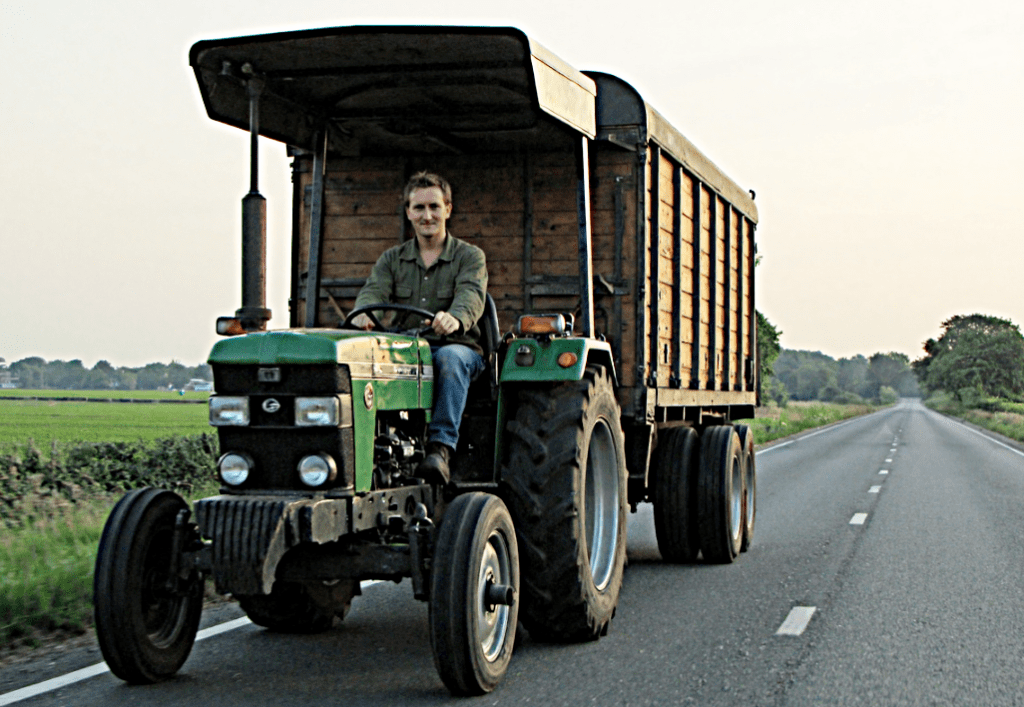 A man driving a tractor and pulling a trailer along a country road 