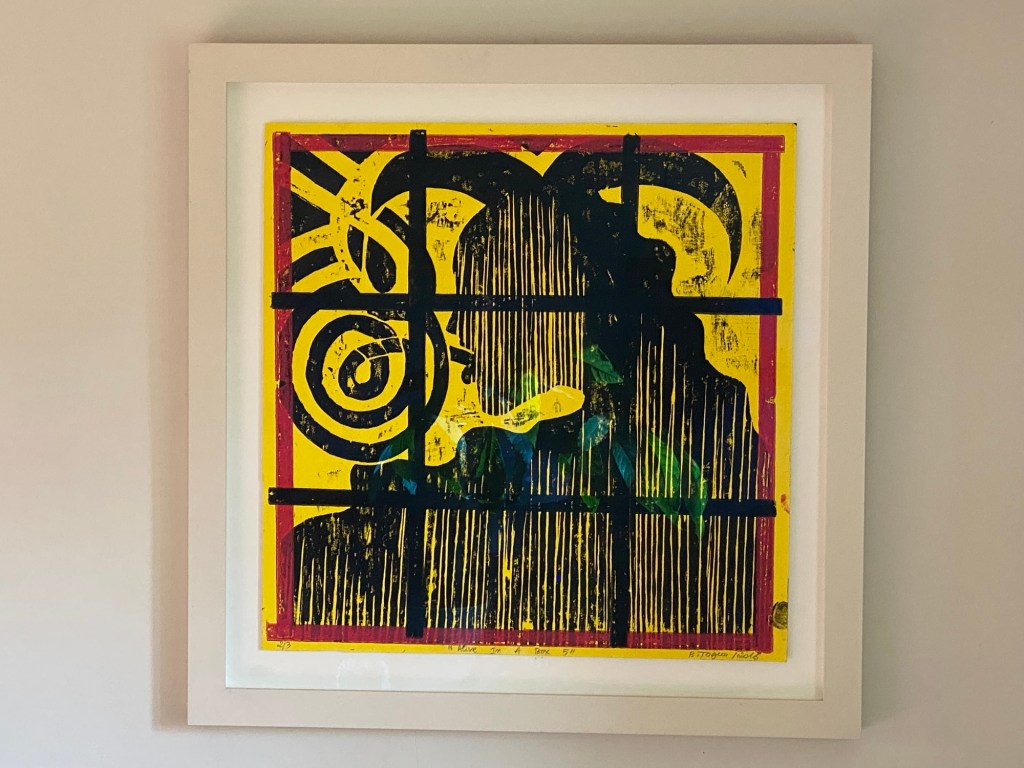 Framed woodblock print artwork featuring abstract shapes and vibrant colors on a yellow background.